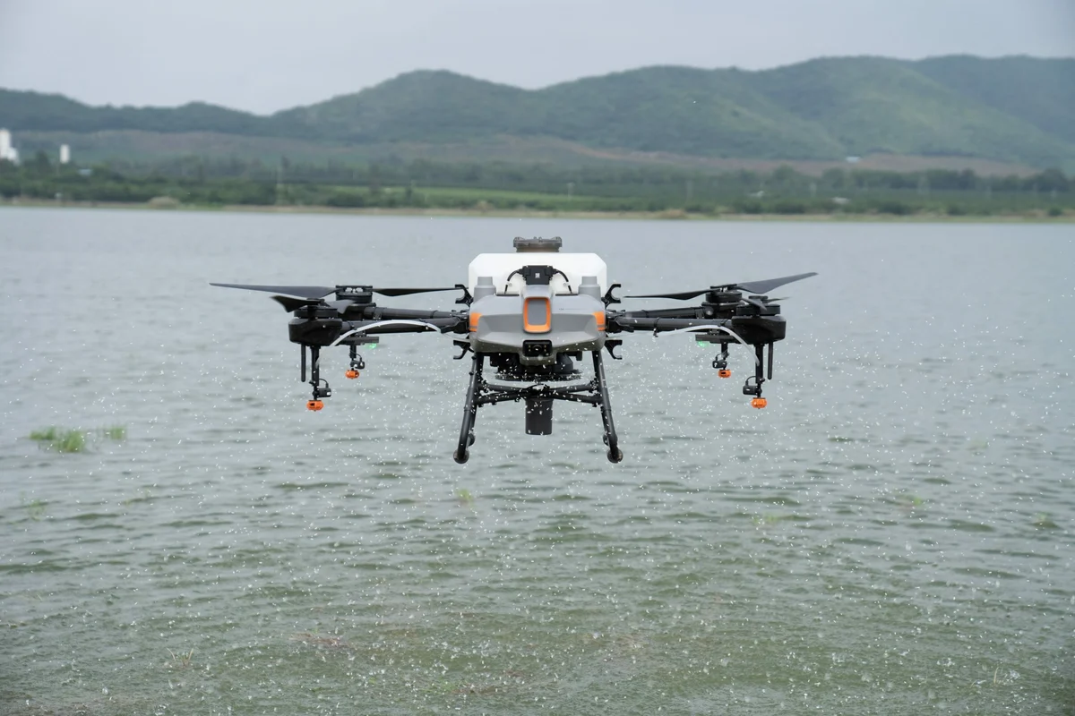 DJI AGRAS T10 flying above water, with its complete airframe and the shoreline visible