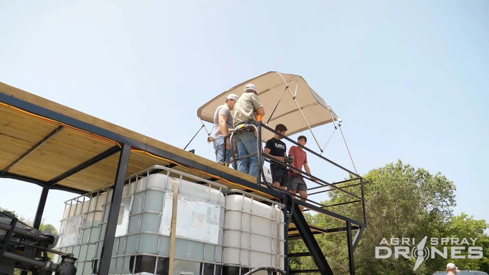 A team reviewing a controller on the raised platform of a field support trailer.