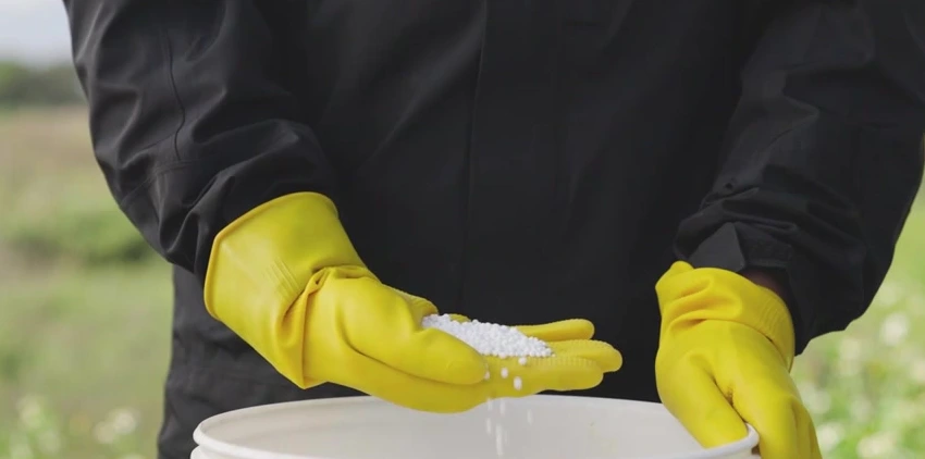 Dry granules held in a gloved hand above a bucket in a DJI material demonstration.